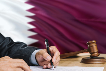 Judge writing on paper in courtroom with Qatar flag background. Wooden gavel of equality theme and...
