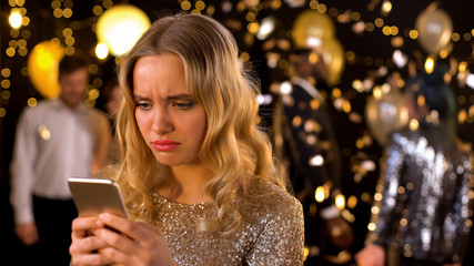 Upset chic female typing message smartphone closeup, dancing people background