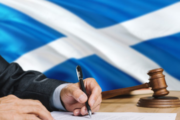 Judge writing on paper in courtroom with Scotland flag background. Wooden gavel of equality theme and legal concept.
