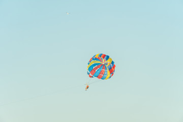 With a multi-colored parachute for parasailing man flying through the air on a background of light blue sky