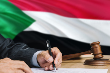 Judge writing on paper in courtroom with Sudan flag background. Wooden gavel of equality theme and legal concept.