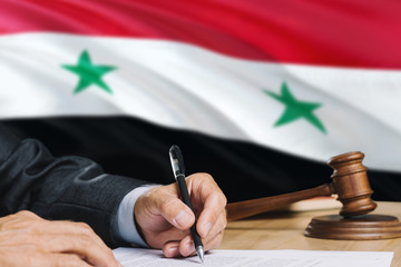 Judge writing on paper in courtroom with Syria flag background. Wooden gavel of equality theme and...