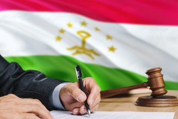 Judge writing on paper in courtroom with Tajikistan flag background. Wooden gavel of equality theme and legal concept.