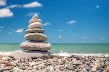 Fototapeta na wymiar pyramid of sea pebbles on the beach against the backdrop of the sea wave in sunny day. concept of balance harmony and meditation. copy space