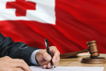 Judge writing on paper in courtroom with Tonga flag background. Wooden gavel of equality theme and legal concept.