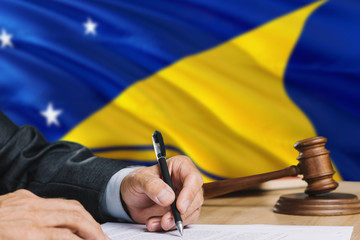 Judge writing on paper in courtroom with Tokelau flag background. Wooden gavel of equality theme and legal concept.