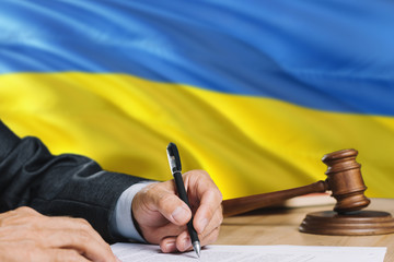 Judge writing on paper in courtroom with Ukraine flag background. Wooden gavel of equality theme and legal concept.