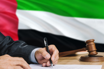 Judge writing on paper in courtroom with United Arab Emirates flag background. Wooden gavel of...