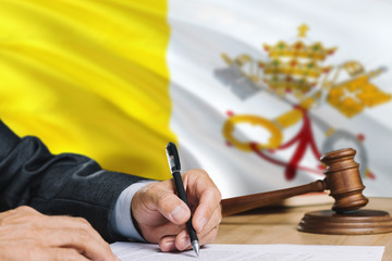 Judge writing on paper in courtroom with Vatican City flag background. Wooden gavel of equality theme and legal concept.
