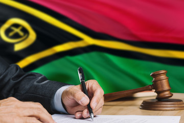 Judge writing on paper in courtroom with Vanuatu flag background. Wooden gavel of equality theme and legal concept.