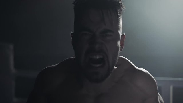 Angry man with boxing gloves screams emotionally at the camera standing on the boxing ring. Slow motion.