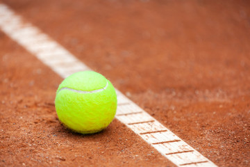 A yellow tennis ball lies on the clay court.