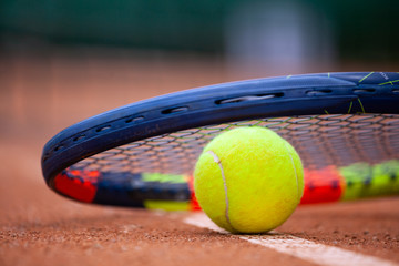 Yellow tennis ball and racket lie on the clay court.