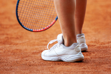Female tennis player legs in tennis shoes standing on a clay court.