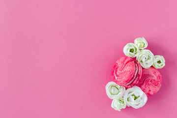 Two pink French macarons with white flowers. Flat lay, place for text.