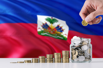 Business man holding coins putting in glass, Haiti flag waving in the background. Finance and...
