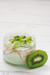 Yogurt with kiwi slices on a wooden white background.