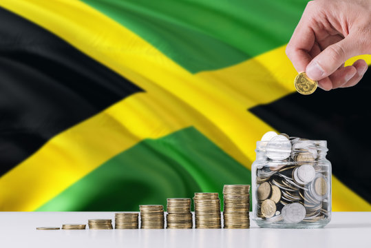 Business man holding coins putting in glass, Jamaica flag waving in the background. Finance and business concept. Saving money.