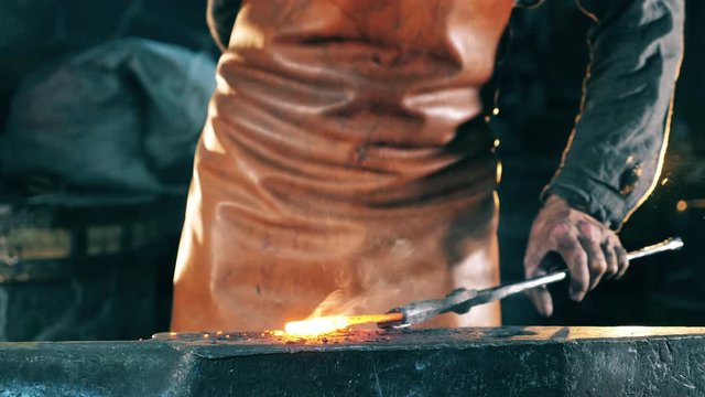 A forger hits hot knife with a metal hammer. Blacksmith forging iron in workshop.