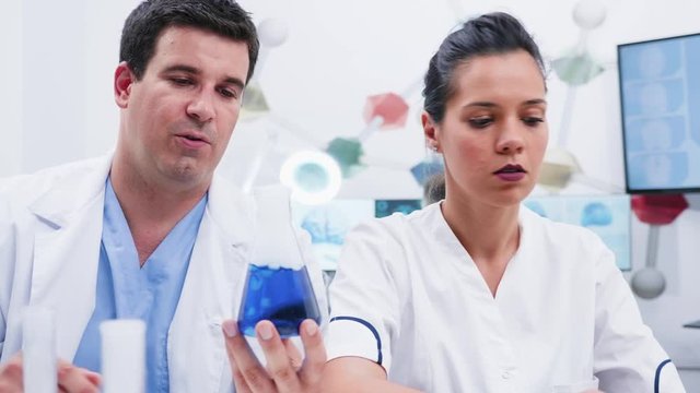 Revealing shot of male and female scientists in modern laboratory looking at a blue smoking liquid