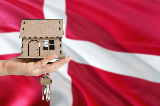 Woman hand holding wooden house and keys with hand. Denmark flag with concept of rent, purchase, insurance, building real estate, eco house.