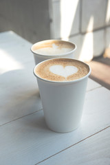 Two white paper cups of coffee on wooden table.