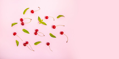 Flat lay of cherries and leaves on a pink background.Top view