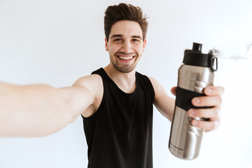 Fototapeta na wymiar Smiling young strong sports man posing isolated over white wall background drinking water take a selfie by camera.