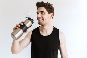 Handsome young strong sports man posing isolated over white wall background drinking water.