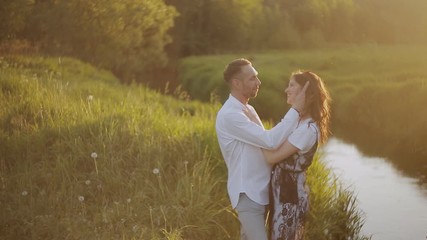 Couple in a park by the river in summer at sunset.