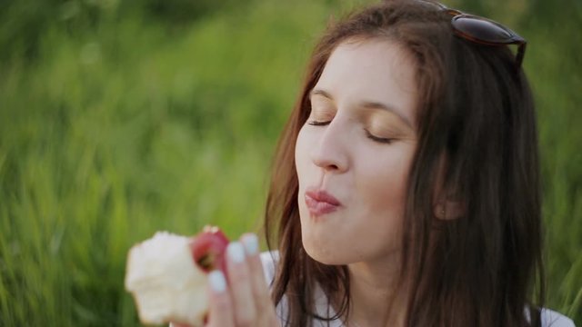 Close-up of a girl biting a red Apple in the Park sitting on the grass.