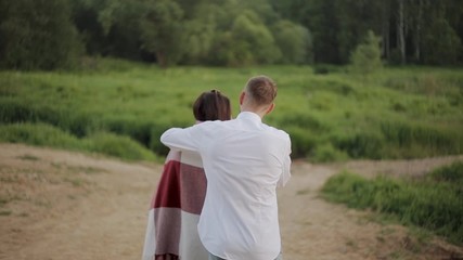 The man wraps the girl in a blanket while walking in the Park in the evening.