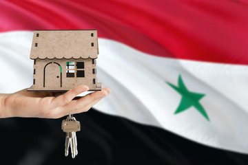 Woman hand holding wooden house and keys with hand. Syria flag with concept of rent, purchase,...