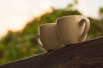 Two cups of coffee on wooden balcony on the background of sunset with beautiful bokeh lights.