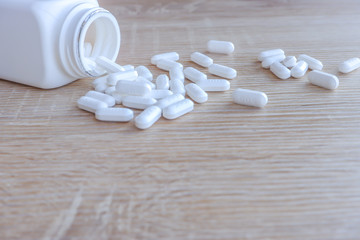 Fototapeta na wymiar White medical pills spilling out of a drug bottle on a wooden backgrounds