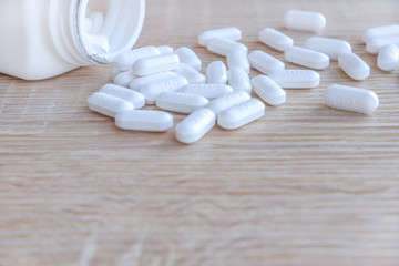 Fototapeta na wymiar White medical pills spilling out of a drug bottle on a wooden backgrounds
