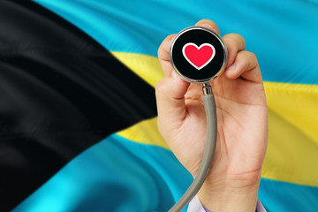 Doctor holding stethoscope with red love heart. National Bahamas flag background. Healthcare system concept, medical theme.