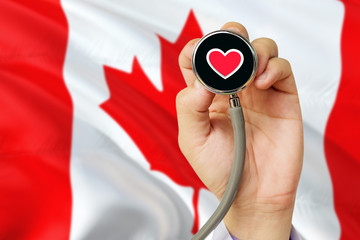 Doctor holding stethoscope with red love heart. National Canada flag background. Healthcare system concept, medical theme.