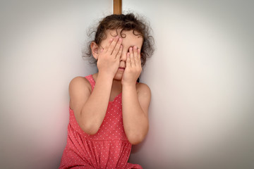 Scared and abused young girl covering her face with hands in fear of domestic violence. Stop child abuse concept.