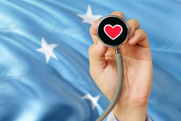 Doctor holding stethoscope with red love heart. National Micronesia flag background. Healthcare system concept, medical theme.