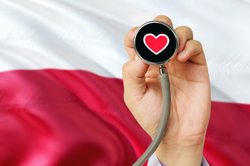 Doctor holding stethoscope with red love heart. National Poland flag background. Healthcare system concept, medical theme.