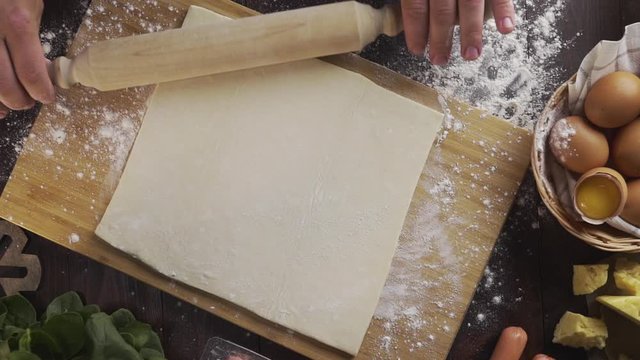 Flat lay shot: chef rolls out the dough with a rolling pin on the kitchen table, table top of the rolling out the puff pastry, eggs and flour, Full HD Prores 422 HQ