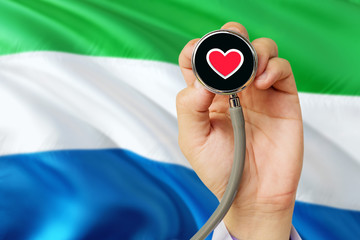 Doctor holding stethoscope with red love heart. National Sierra Leone flag background. Healthcare system concept, medical theme.