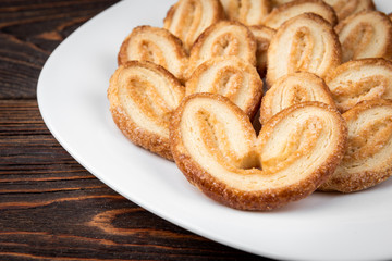 Palmier cookies or puff pastry ears on dark wooden background.