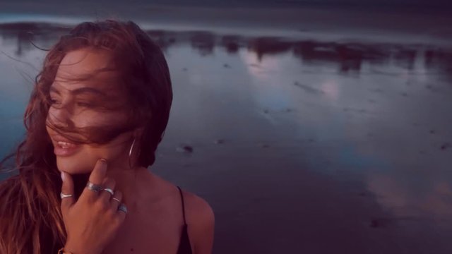 Portrait of sensual brunette girl in black dress posing on the black sand beach - video in slow motion