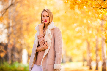 Fall concept - beautiful woman drinking coffee in autumn park under fall foliage