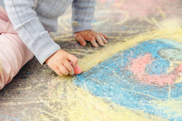 Child draws hand in colored chalk drawing on pavement. Top view