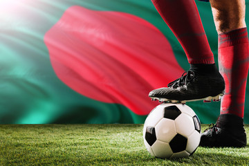 Close up legs of Bangladesh football team player in red socks, shoes on soccer ball at the free kick or penalty spot playing on grass.