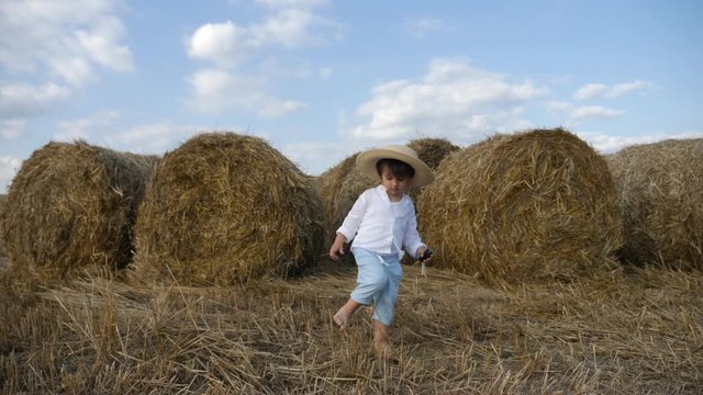 boy in a white shirt and a straw hat is barefoot on a sloping field