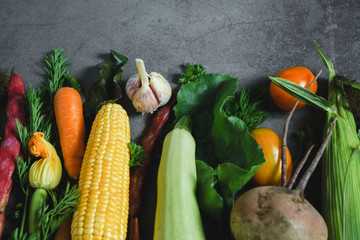 Assorted fresh vegetables on a black background. Corn, tomatoes, zucchini, carrot, beetroot, garlic, bean. Food concept. Flat lay, top view, copy space